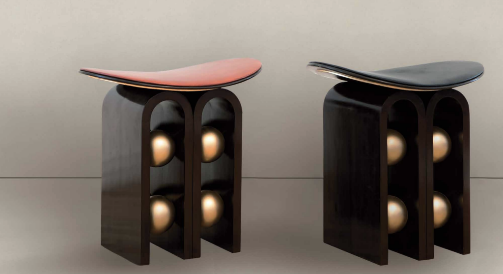 Curved Seat Wooden Stools with Gold Spheres – A pair of sculptural stools featuring a dark wooden base with arched legs and embedded gold spheres. The seats are curved and come in two finishes: one with a reddish-brown leather top and the other with a black leather top, giving them a sleek, modern look.