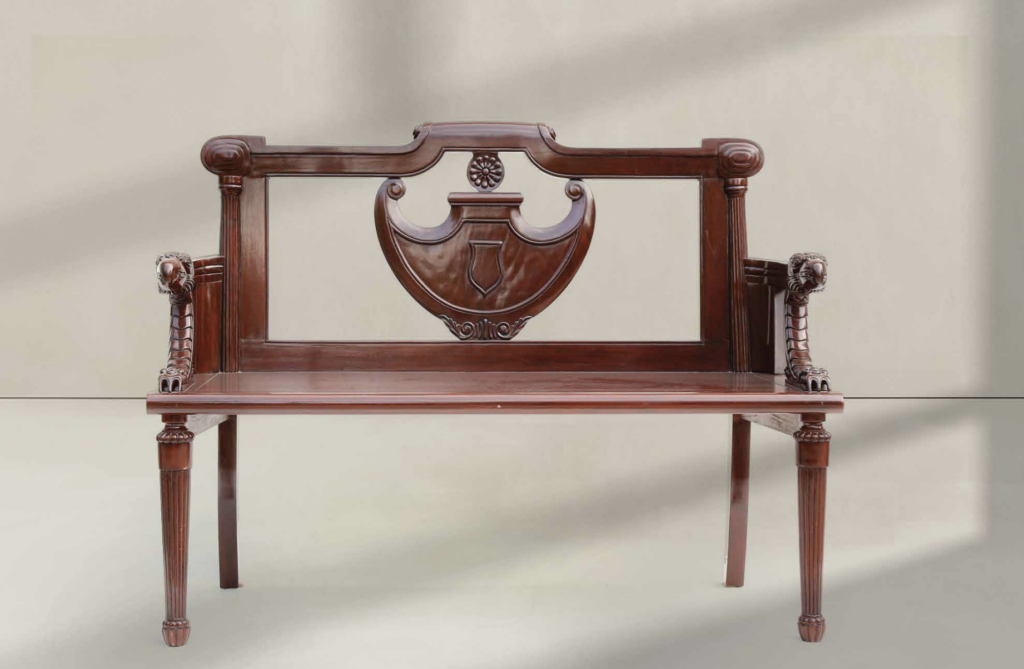 Classic Wooden Bench with Carved Details – A dark wood bench featuring a traditional carved backrest with a shield-like centerpiece and lion head armrests. Its ornate craftsmanship gives it an antique and regal feel.