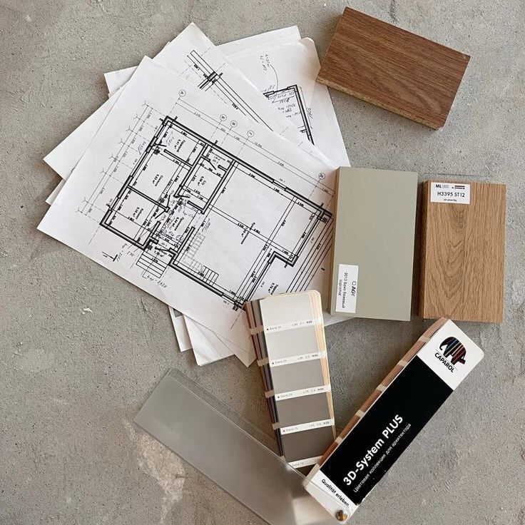 Top-down flat lay of architectural floor plans, wood finish samples, paint swatches, and a color deck on a concrete surface.